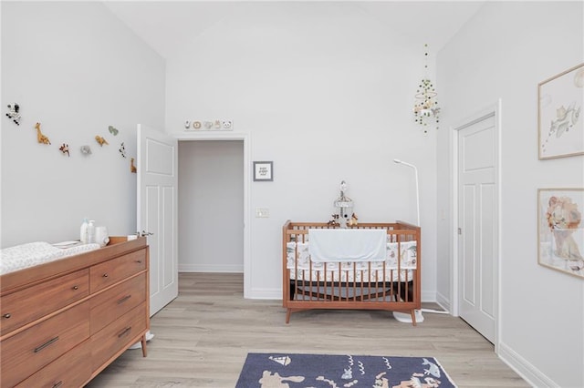 bedroom featuring high vaulted ceiling, light hardwood / wood-style flooring, and a crib