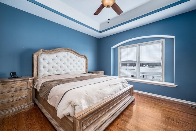 bedroom with ceiling fan, hardwood / wood-style flooring, and a tray ceiling