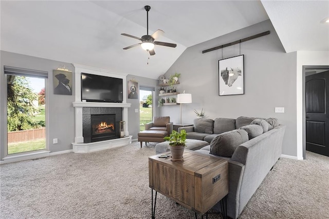 living room with a tiled fireplace, ceiling fan, vaulted ceiling, and carpet