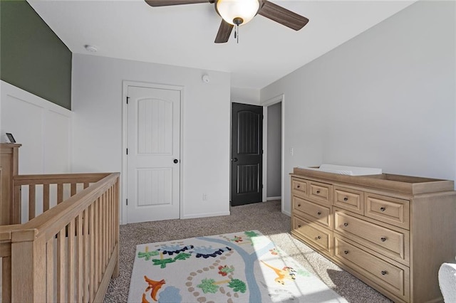 bedroom featuring a nursery area, ceiling fan, and light colored carpet