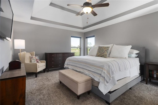 carpeted bedroom with a raised ceiling and ceiling fan