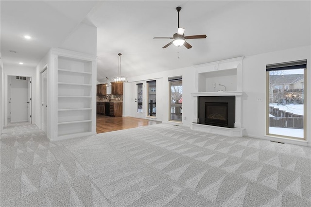 unfurnished living room with ceiling fan, light carpet, and built in shelves