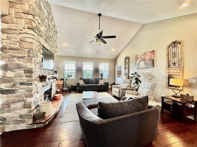 living room featuring ceiling fan, dark hardwood / wood-style floors, high vaulted ceiling, and a stone fireplace