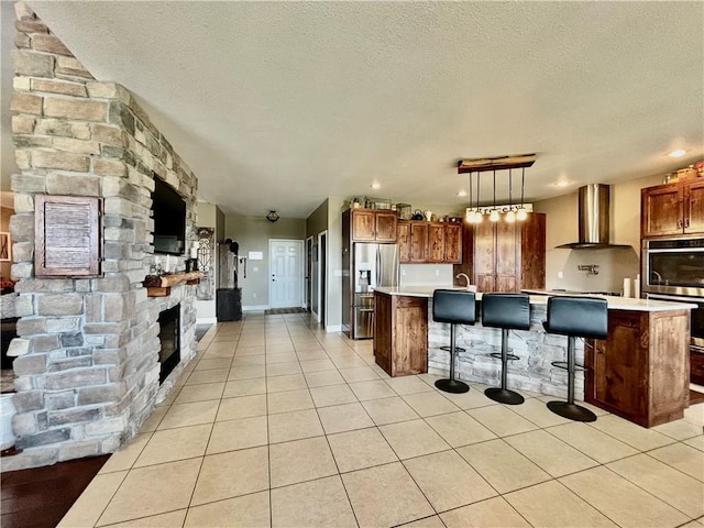 kitchen with appliances with stainless steel finishes, a breakfast bar, pendant lighting, a kitchen island with sink, and wall chimney range hood