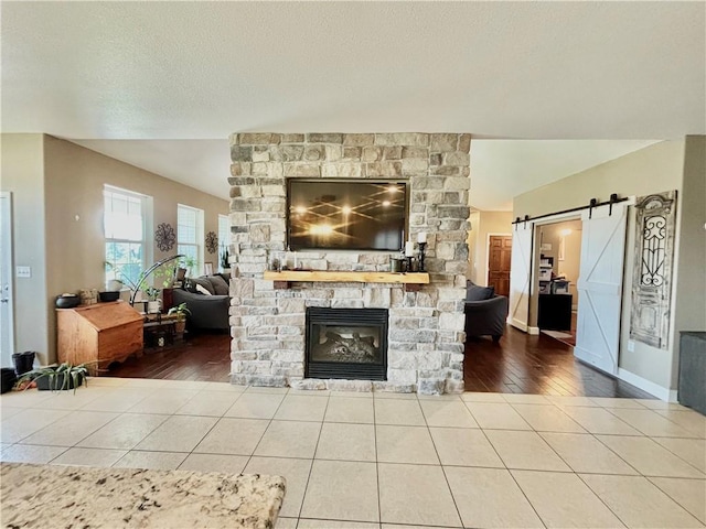 tiled living room with a stone fireplace, a barn door, and a textured ceiling