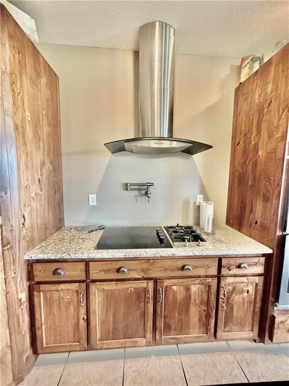 kitchen featuring wall chimney range hood, light tile patterned floors, black stovetop, light stone countertops, and a textured ceiling