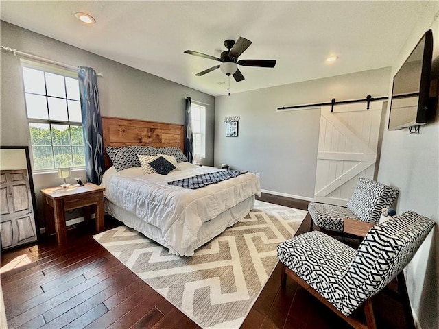 bedroom featuring multiple windows, dark wood-type flooring, a barn door, and ceiling fan