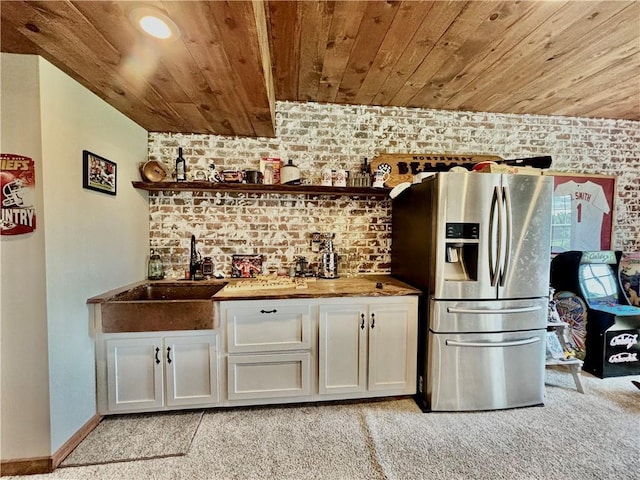 bar with butcher block countertops, white cabinetry, stainless steel refrigerator with ice dispenser, brick wall, and wooden ceiling