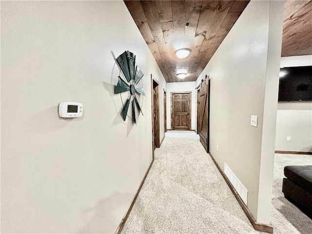 hallway with light colored carpet, a barn door, and wooden ceiling