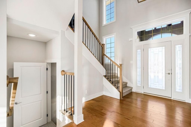 entrance foyer with hardwood / wood-style floors, stairway, a towering ceiling, and baseboards