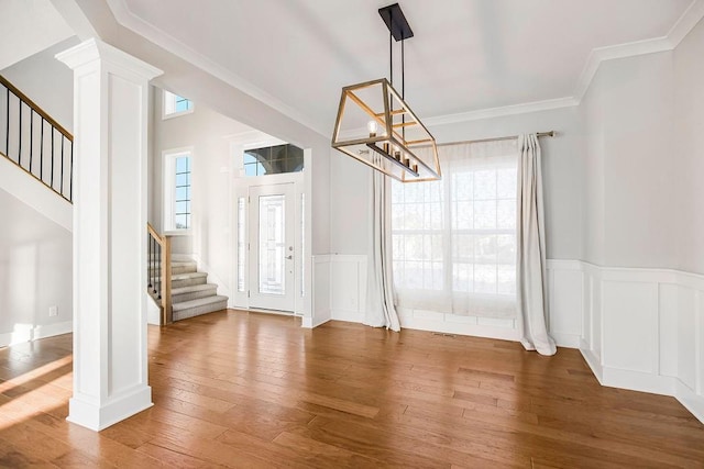 unfurnished dining area featuring crown molding, stairway, a wainscoted wall, decorative columns, and hardwood / wood-style flooring