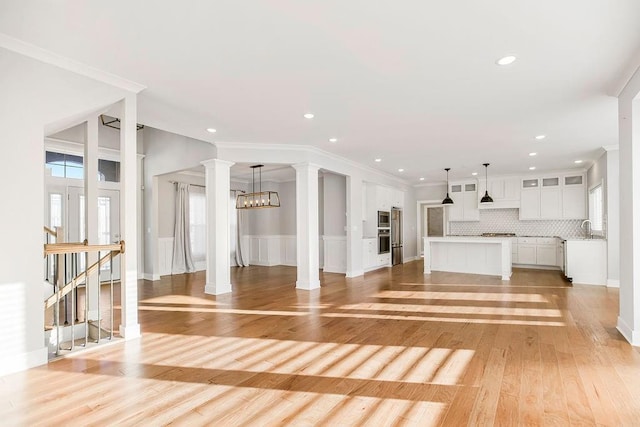 unfurnished living room featuring ornamental molding, decorative columns, light wood-type flooring, and a sink