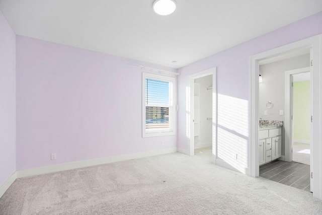 unfurnished bedroom with baseboards, light colored carpet, and ensuite bath