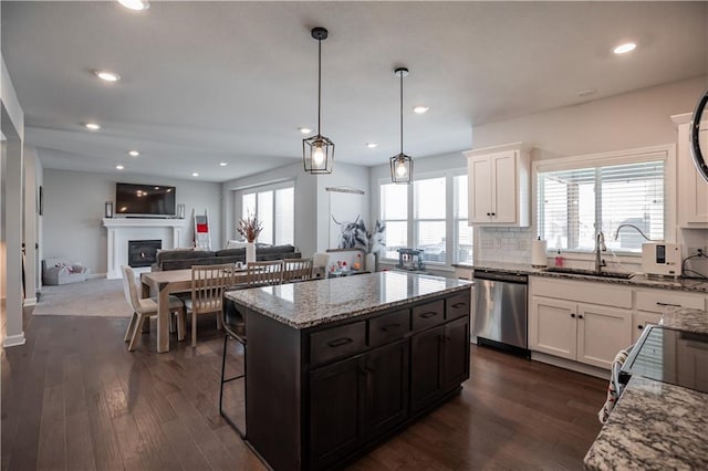 kitchen with stainless steel dishwasher, sink, decorative light fixtures, a center island, and white cabinetry