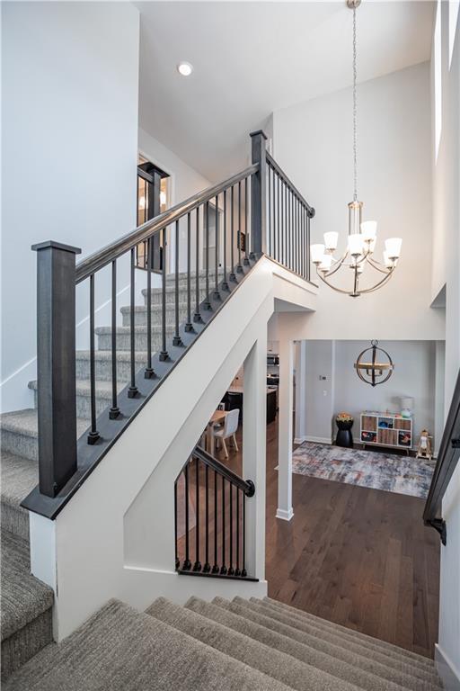 stairs featuring wood-type flooring, a high ceiling, and an inviting chandelier