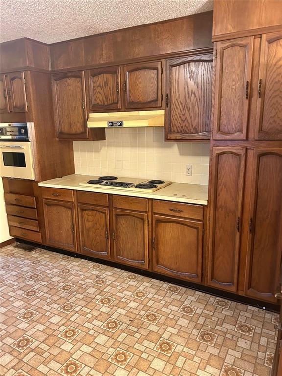 kitchen featuring tasteful backsplash, light countertops, a textured ceiling, white appliances, and under cabinet range hood