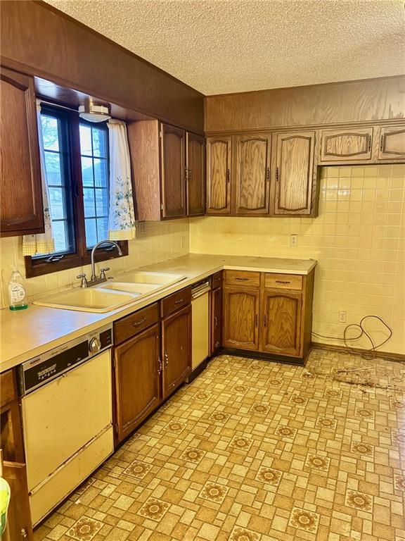 kitchen featuring a sink, a textured ceiling, light countertops, and dishwasher