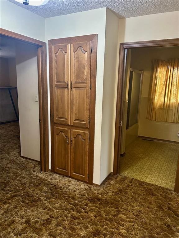 hall featuring a textured ceiling and dark colored carpet