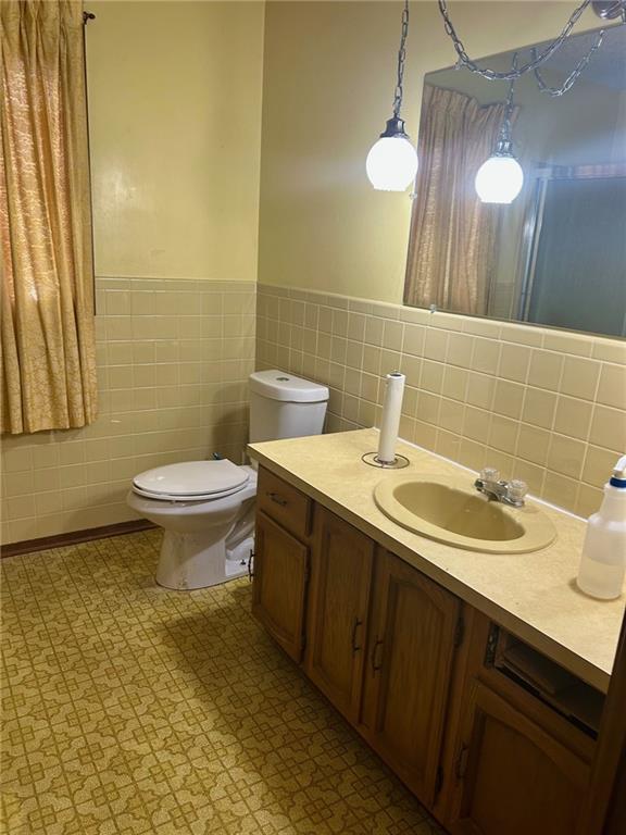 bathroom with toilet, wainscoting, tile walls, and vanity