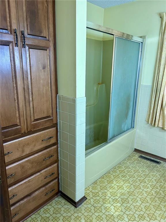 bathroom with visible vents, bath / shower combo with glass door, tile walls, and tile patterned floors