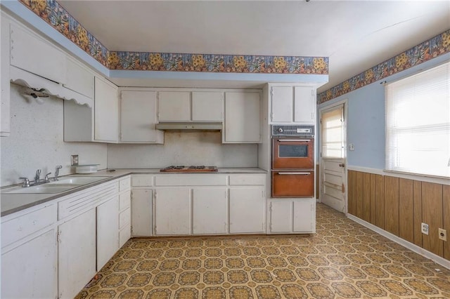 kitchen with sink, stainless steel gas cooktop, wall oven, wooden walls, and white cabinets