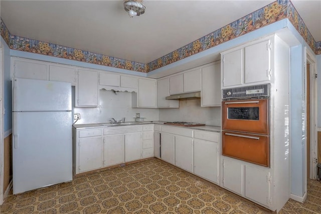 kitchen with white fridge, black oven, white cabinetry, and sink