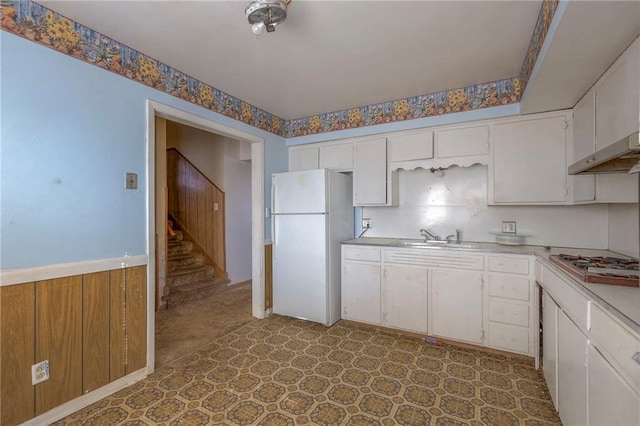 kitchen featuring sink, white refrigerator, white cabinets, stainless steel gas stovetop, and wood walls