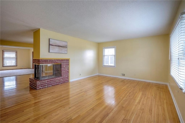 unfurnished living room featuring light wood-type flooring, a brick fireplace, baseboards, and a textured ceiling