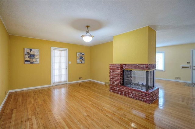 unfurnished living room featuring a fireplace, visible vents, a textured ceiling, baseboards, and hardwood / wood-style flooring