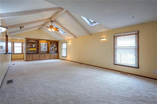 empty room featuring vaulted ceiling with skylight, baseboards, visible vents, light colored carpet, and a textured ceiling