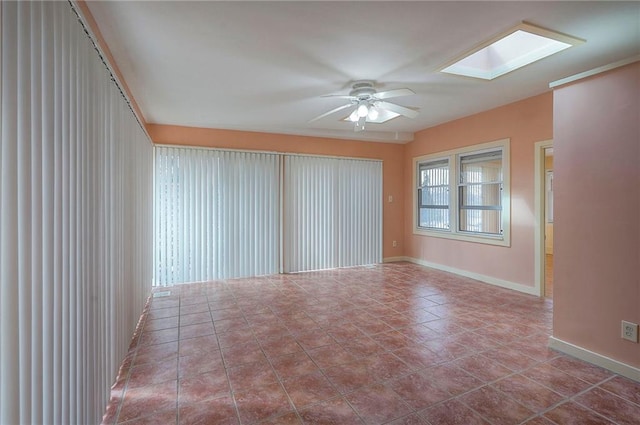 empty room with a ceiling fan, a skylight, baseboards, and tile patterned floors