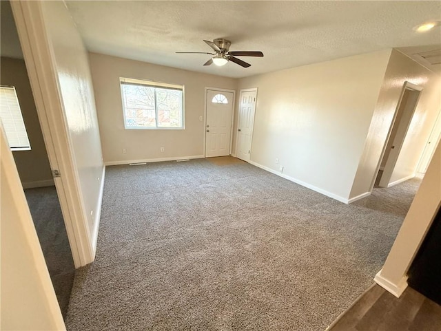 spare room with a textured ceiling, dark carpet, and ceiling fan