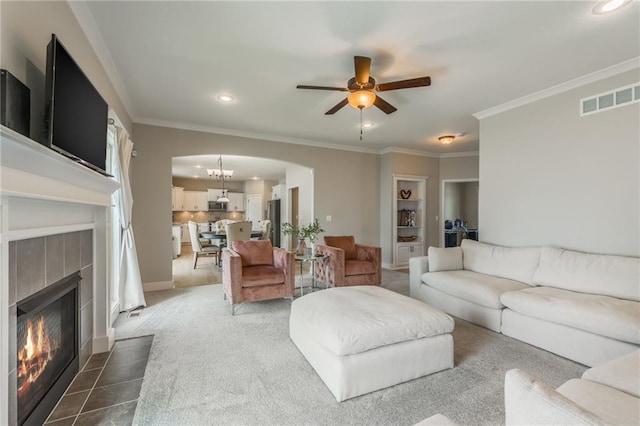 carpeted living room featuring a tile fireplace, ceiling fan with notable chandelier, and crown molding