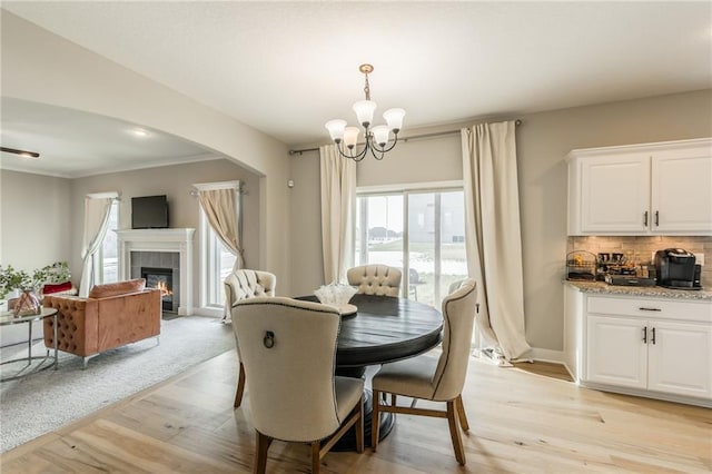 dining room with an inviting chandelier, ornamental molding, a fireplace, and light hardwood / wood-style flooring