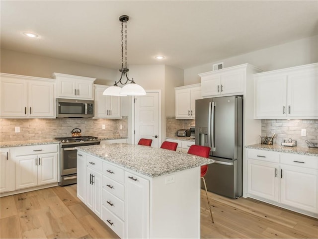 kitchen with a kitchen bar, hanging light fixtures, appliances with stainless steel finishes, a kitchen island, and white cabinets