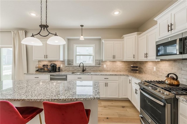 kitchen featuring appliances with stainless steel finishes, decorative light fixtures, sink, white cabinets, and light stone counters