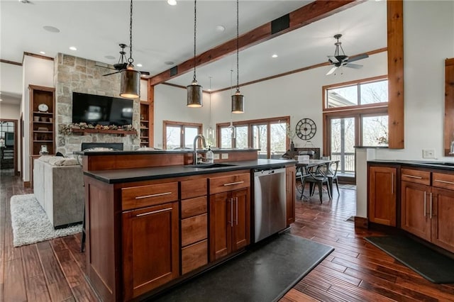 kitchen with a fireplace, dark countertops, stainless steel dishwasher, open floor plan, and a sink