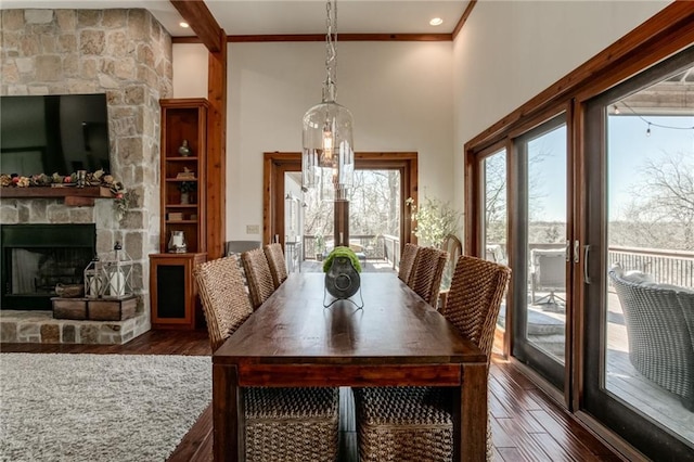 dining space with crown molding, dark wood-style flooring, a fireplace, and a high ceiling