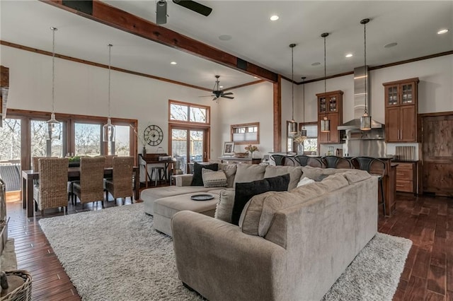 living room featuring beam ceiling, a towering ceiling, a ceiling fan, dark wood-type flooring, and ornamental molding