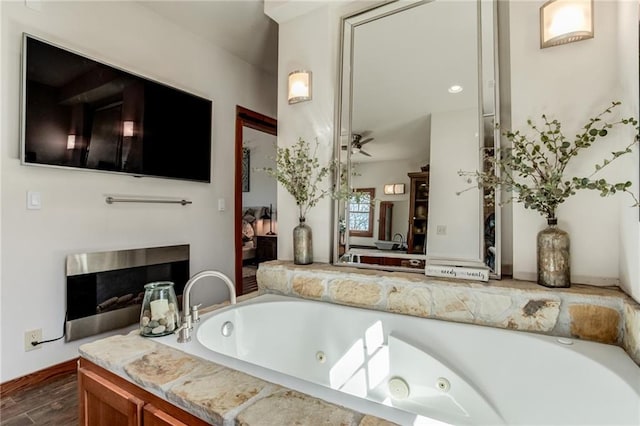 bathroom with ensuite bath, ceiling fan, a tub with jets, wood finished floors, and a fireplace