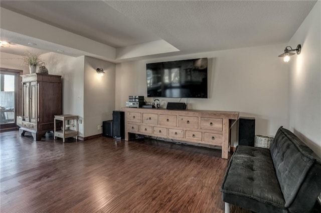 living area featuring a tray ceiling, dark wood-style flooring, a textured ceiling, and baseboards