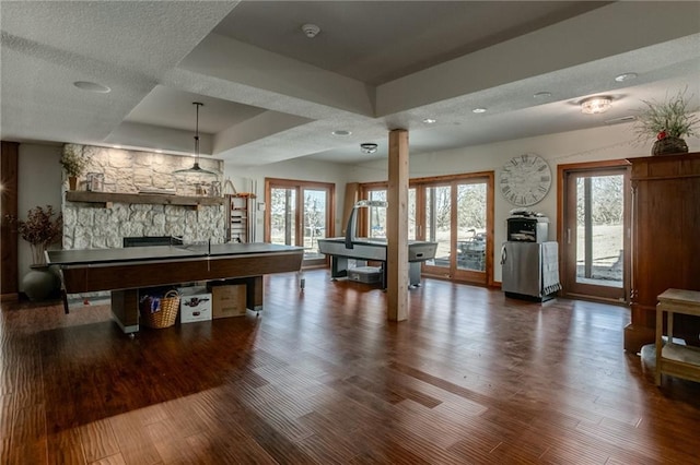 recreation room featuring a tray ceiling, a stone fireplace, wood finished floors, and ornate columns