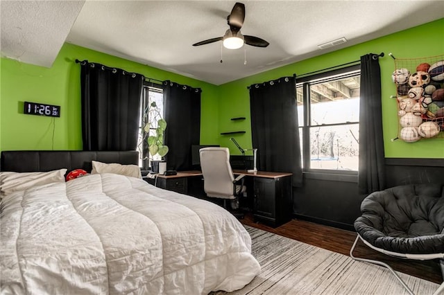 bedroom with a ceiling fan, visible vents, a textured ceiling, and wood finished floors