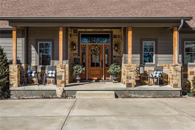 doorway to property featuring a porch, stone siding, and a shingled roof