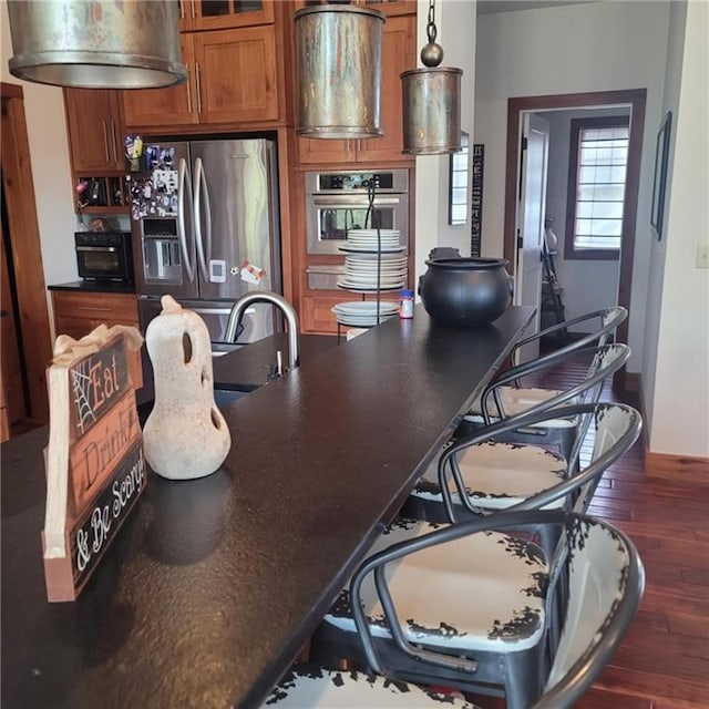 kitchen with appliances with stainless steel finishes, dark countertops, brown cabinets, and wood finished floors