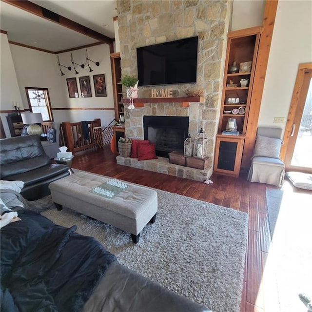 living area with plenty of natural light, wood-type flooring, built in shelves, and a stone fireplace