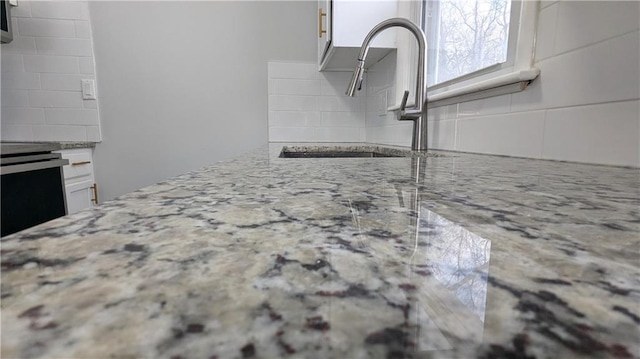 interior details featuring sink, white cabinets, backsplash, range, and light stone counters