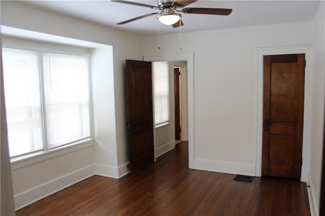 unfurnished room featuring a wealth of natural light, ceiling fan, and dark wood-type flooring