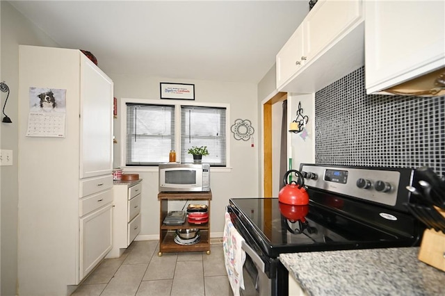 kitchen with light tile patterned floors, tasteful backsplash, white cabinetry, and stainless steel electric stove