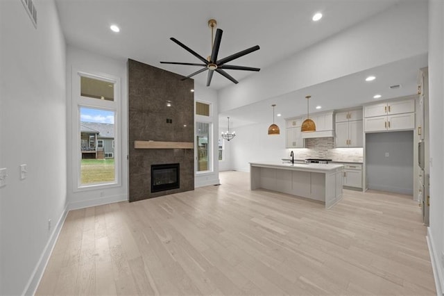 kitchen with white cabinetry, an island with sink, pendant lighting, light hardwood / wood-style floors, and decorative backsplash